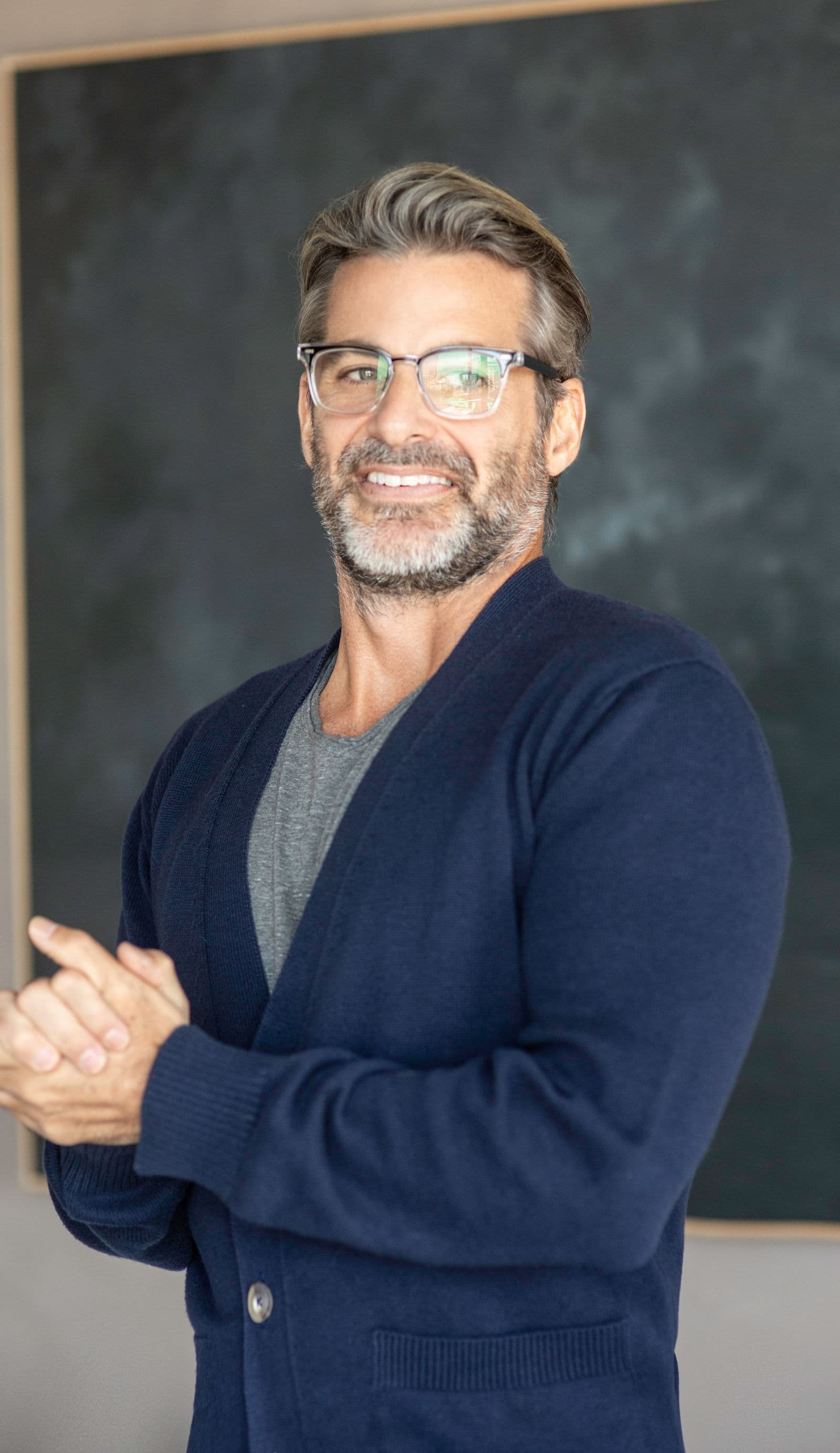 Jim Curtis in glasses and a navy cardigan, hands clasped, mid conversation