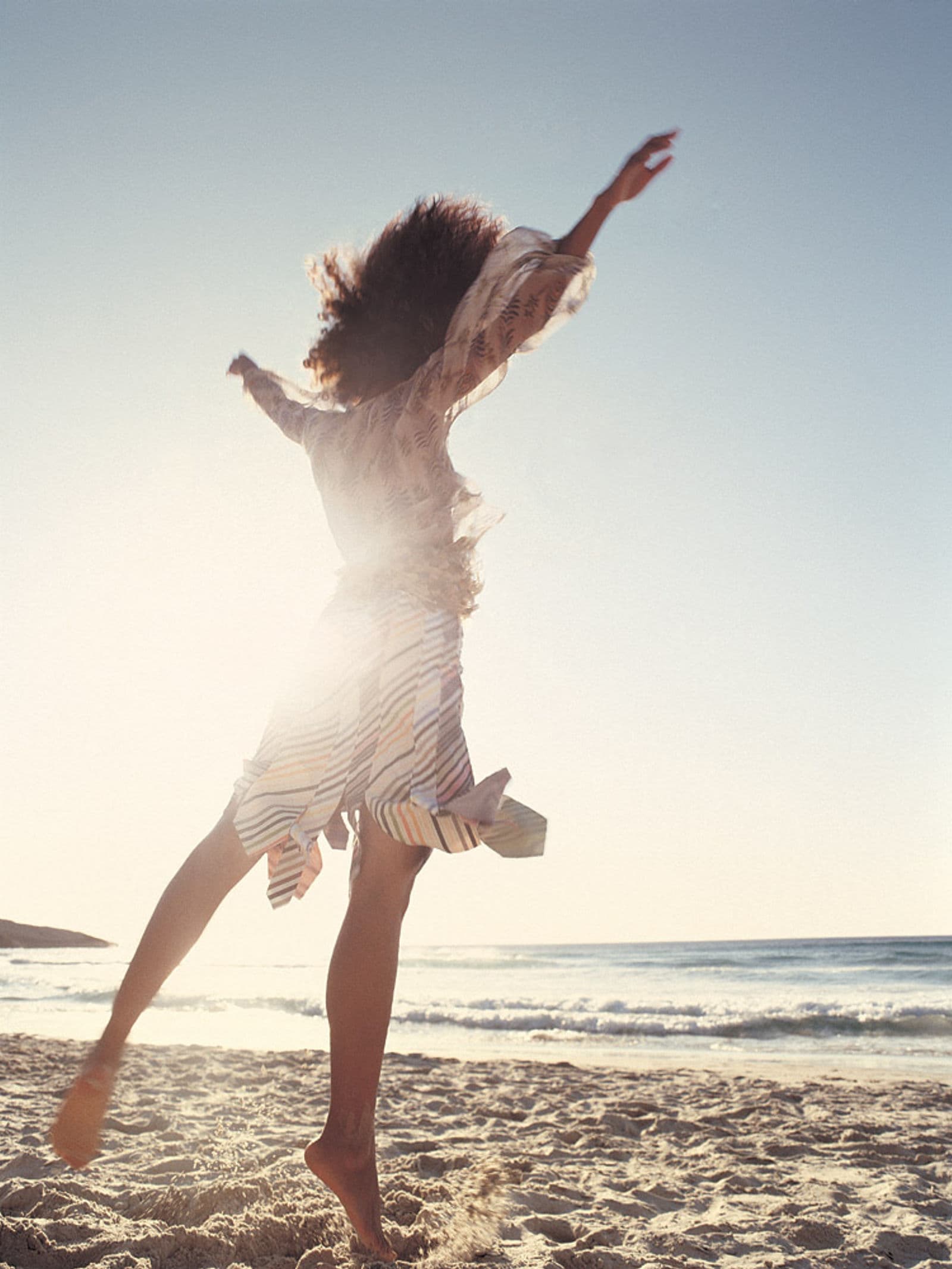 A woman dancing barefoot on a sunlit beach