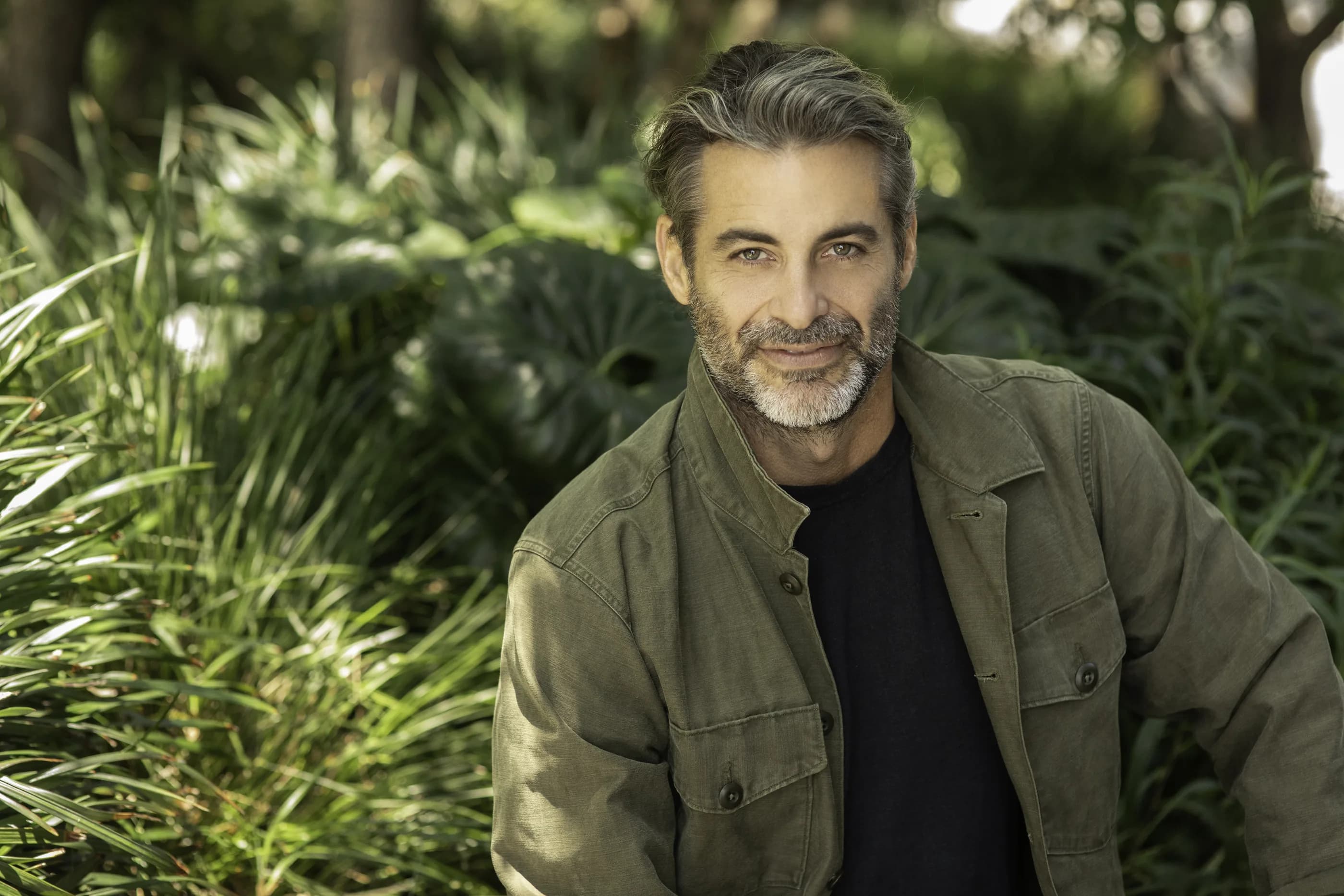 Jim Curtis in an olive jacket, standing among tropical greenery