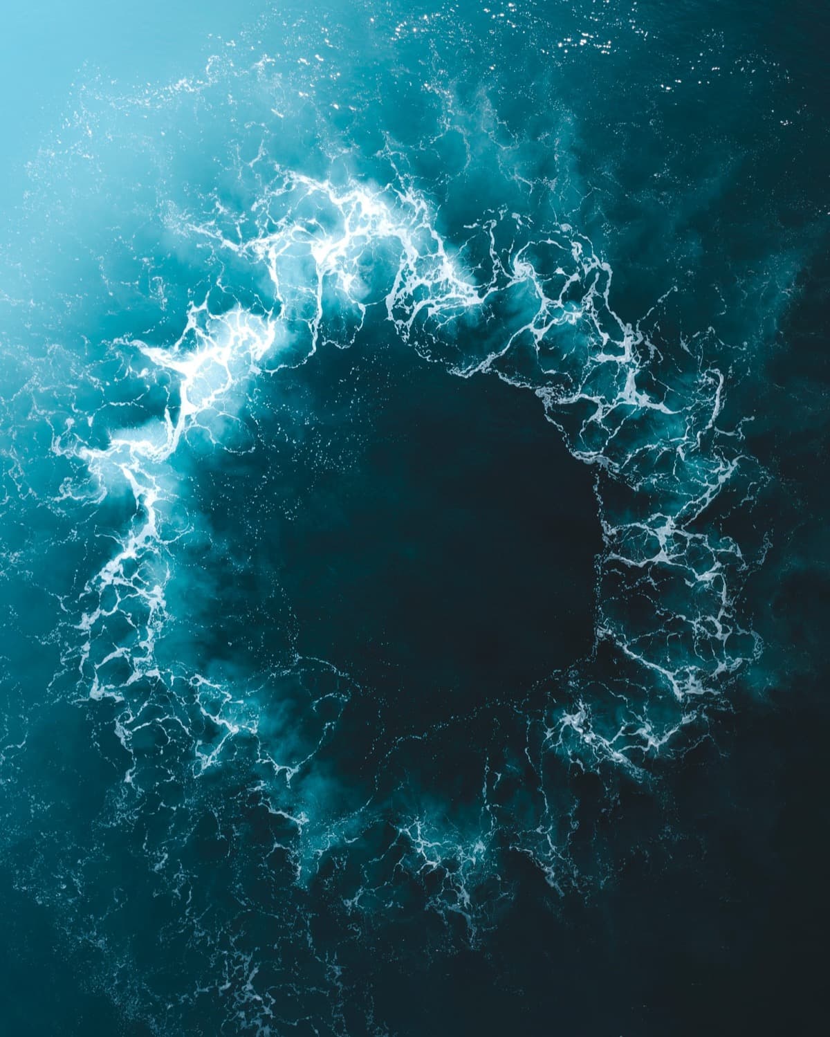 Aerial view of turquoise ocean water curling into a wide circle